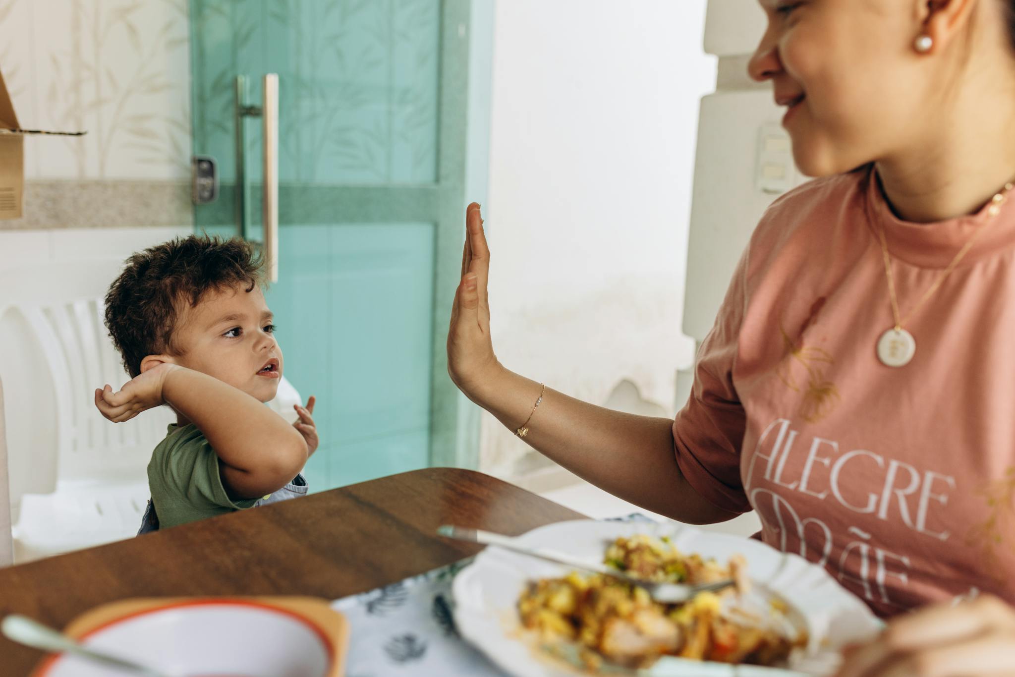 Mother and child enjoying a meal together, bonding through a high-five moment.